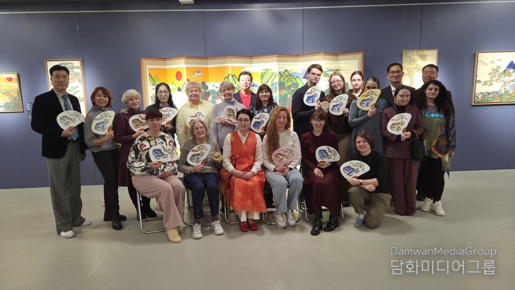 Participants in a traditional Korean folk painting masterclass held at the National Museum of Art in Belarus pose for a commemorative photo holding their completed tiger fan artwork. Professor Lee Mi-hyung of Myongji University, who led the lecture, is in the center, while the Korean delegation and officials from the Belarusian Museum of Art are on either side.